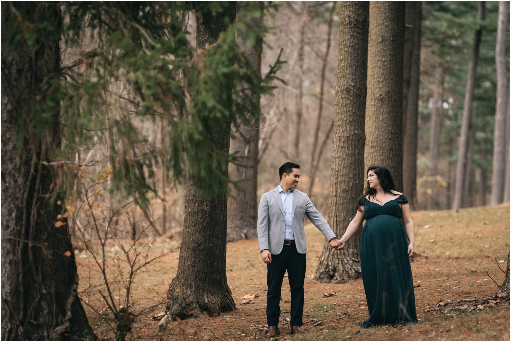 pregnant woman and man hold hands in the woods wearing an emerald green maternity dress