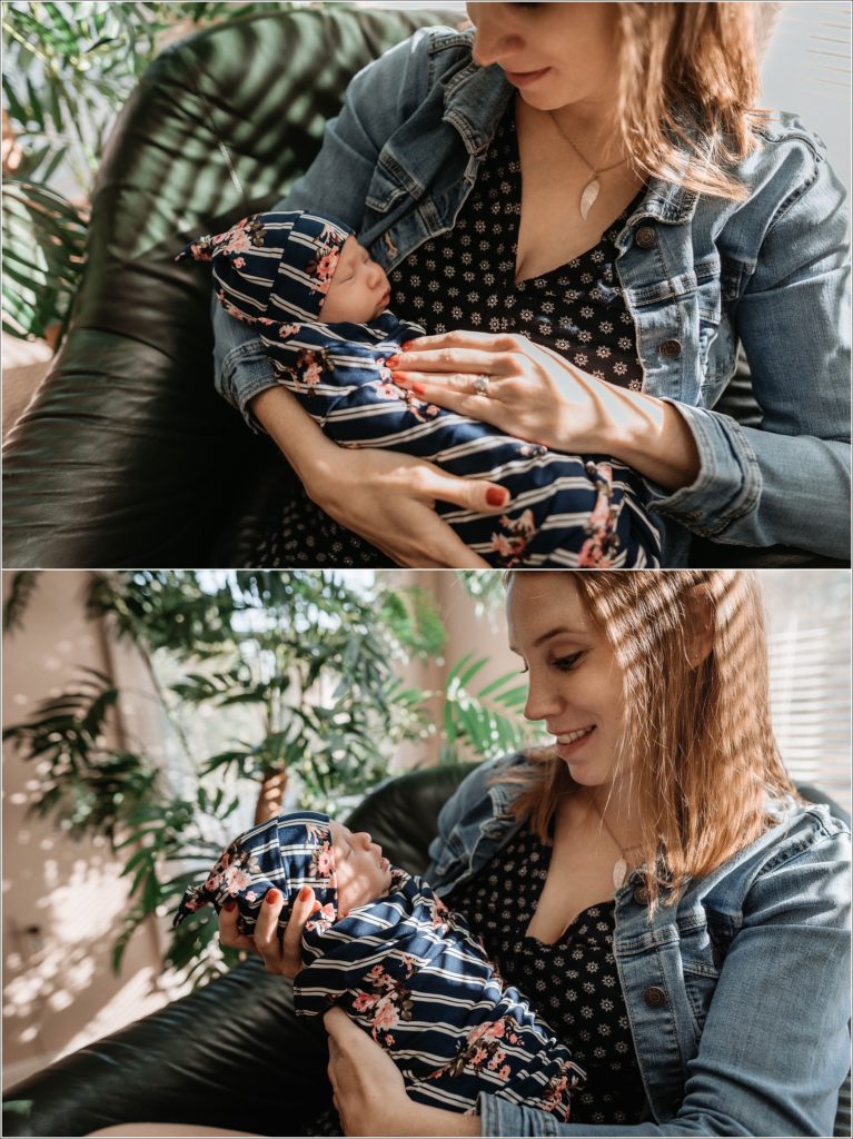 mother holds newborn baby by window with green plant in background
