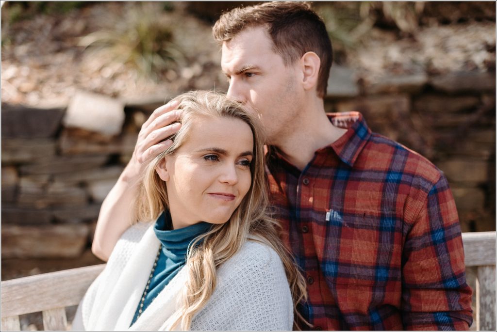 couple poses in asian garden for national arboretum engagement photos in red plaid and a teal turtleneck and white sweater