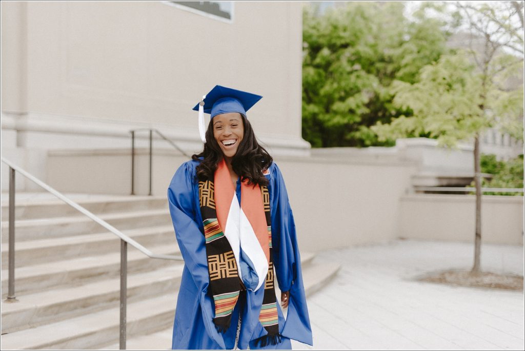 american university grad in blue cap and gown walks down stairs in graduation photos