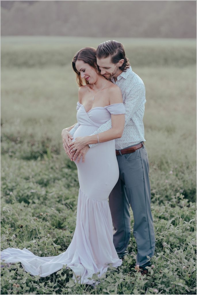 Pregnant woman in lilac maternity dress in Urbana Villages field with her husband