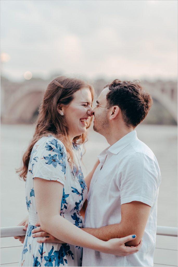 Engaged Couple snuggles by the Georgetown Waterfront in white linen outfits with blue flowers