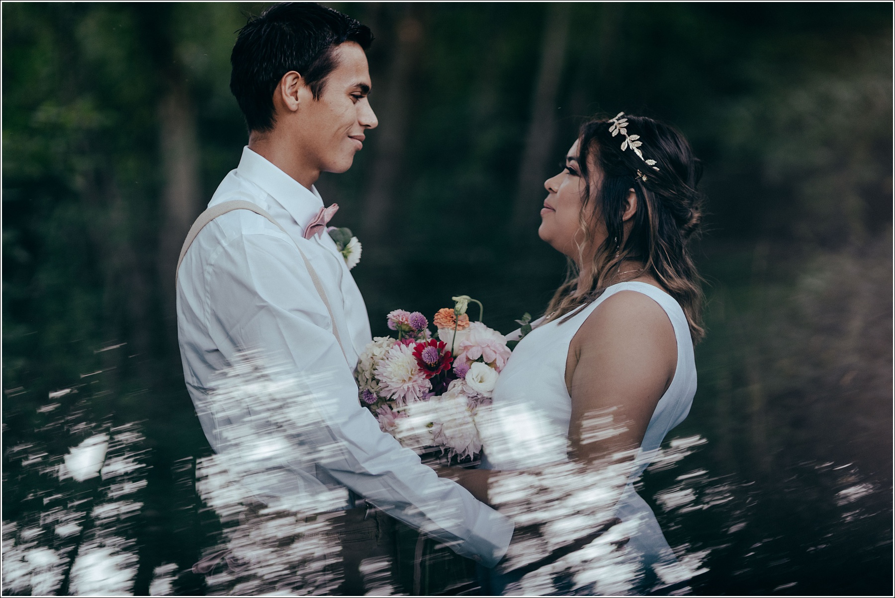 Bride and groom face one another in the woods with bouquet