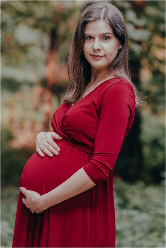 pregnant woman poses at sligo creek trail in burgundy maternity dress