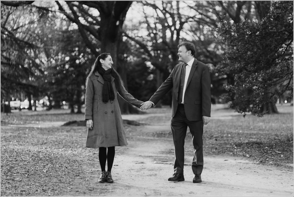 couple holds hands and looks at each other on walking path in Lincoln Park DC elopement black and white image