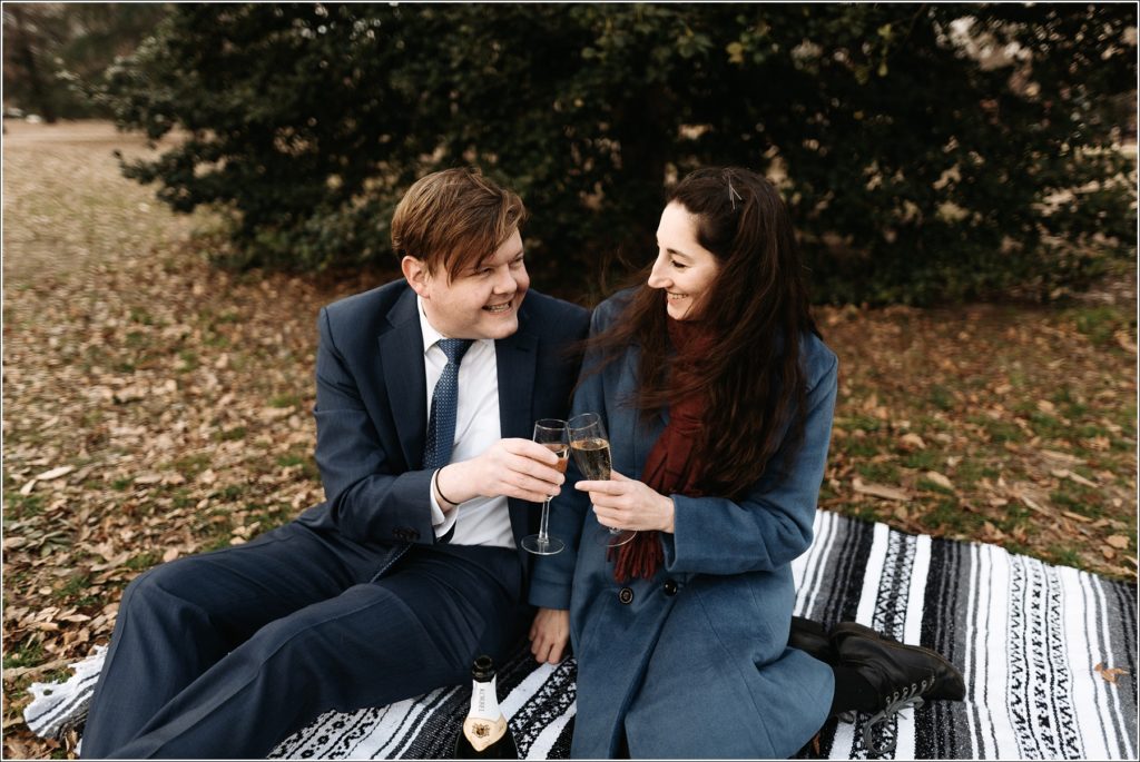 couple does a champagne toast wearing blue sitting on blanket for DC elopement