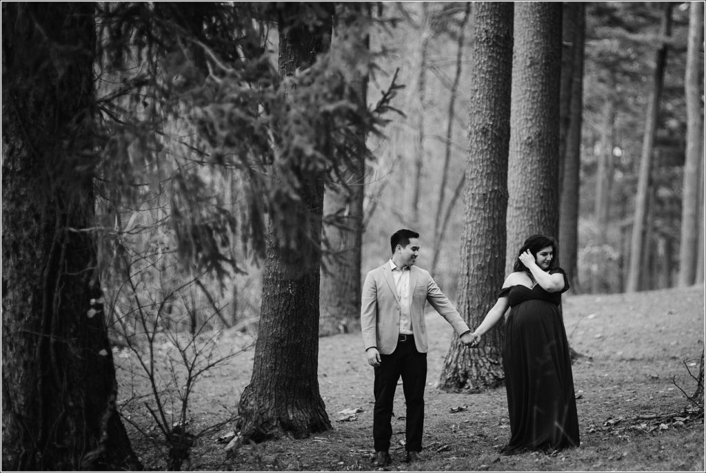 pregnant woman and man hold hands in the woods black and white