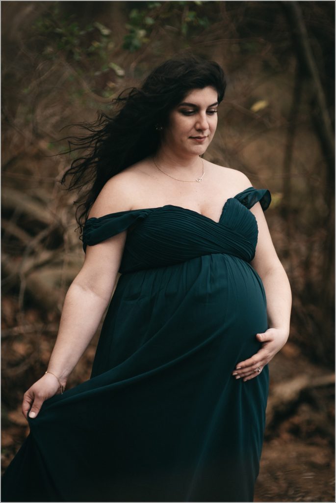 pregnant woman in emerald green dress holds her belly and looks down with hair flowing