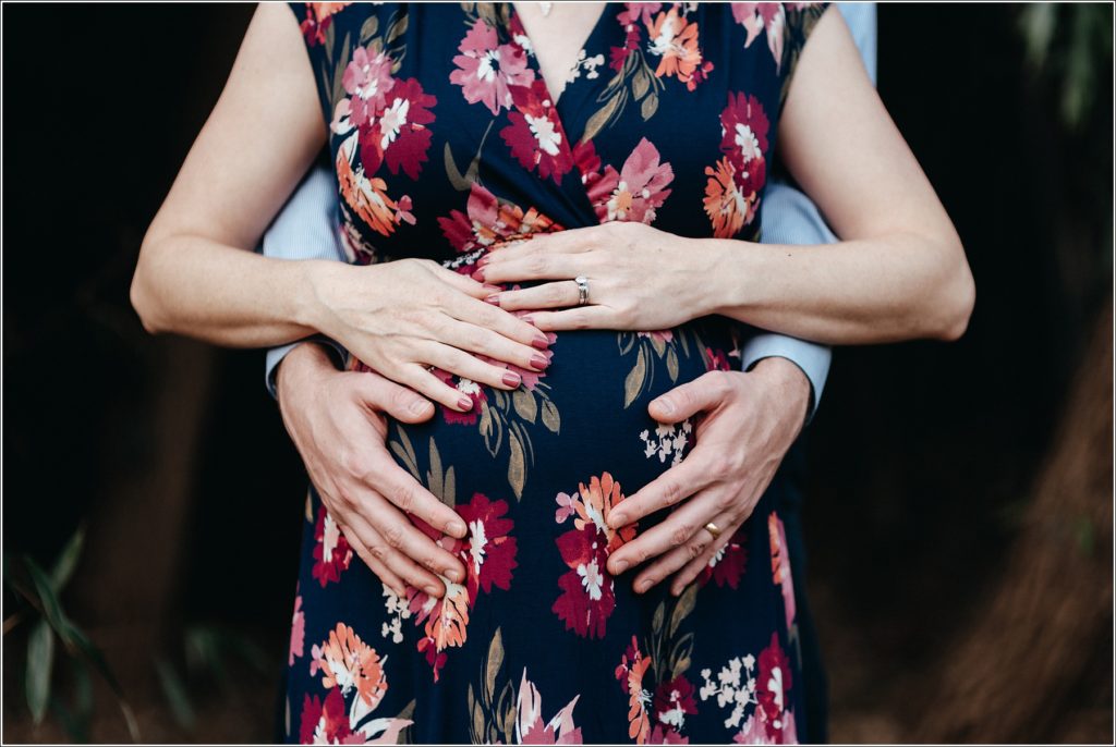 four hands on a pregnant belly woman wearing floral print dress