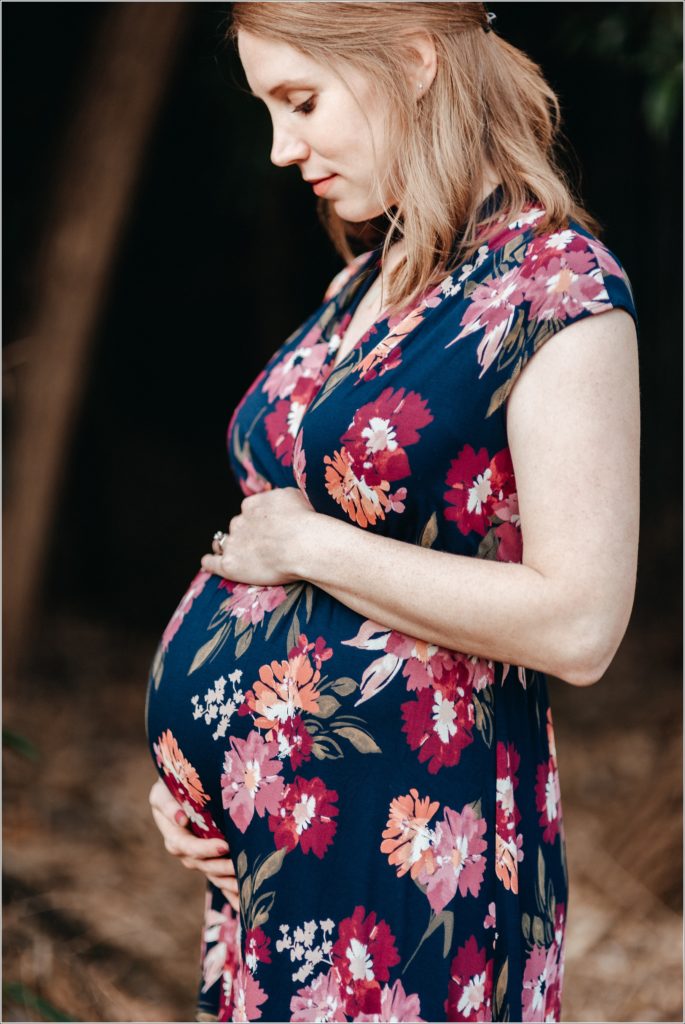 pregnant woman poses profile holding her belly in a floral dress with a black background