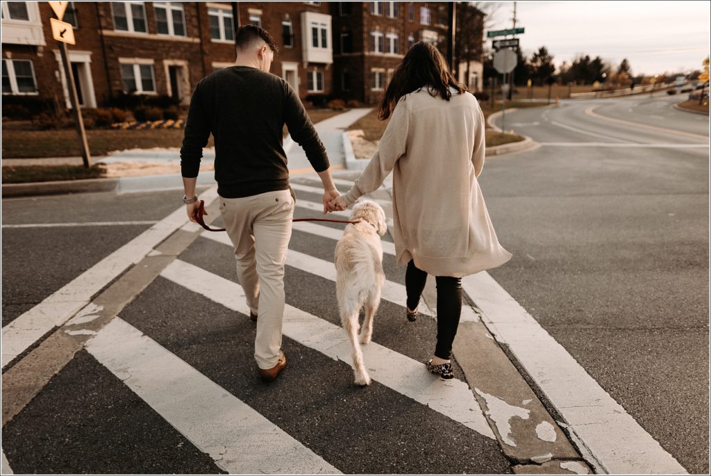 man and woman walk across the street with their labradoodle in between
