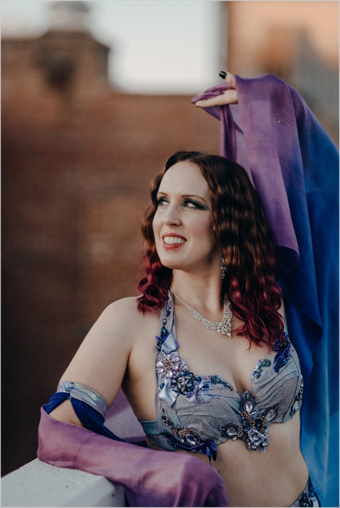 belly dancer photoshoot in blue and purple costume with red brick backdrop