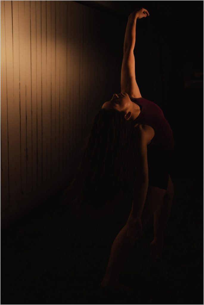 dc dancer dances in yellow light against white barn with shadows behind her