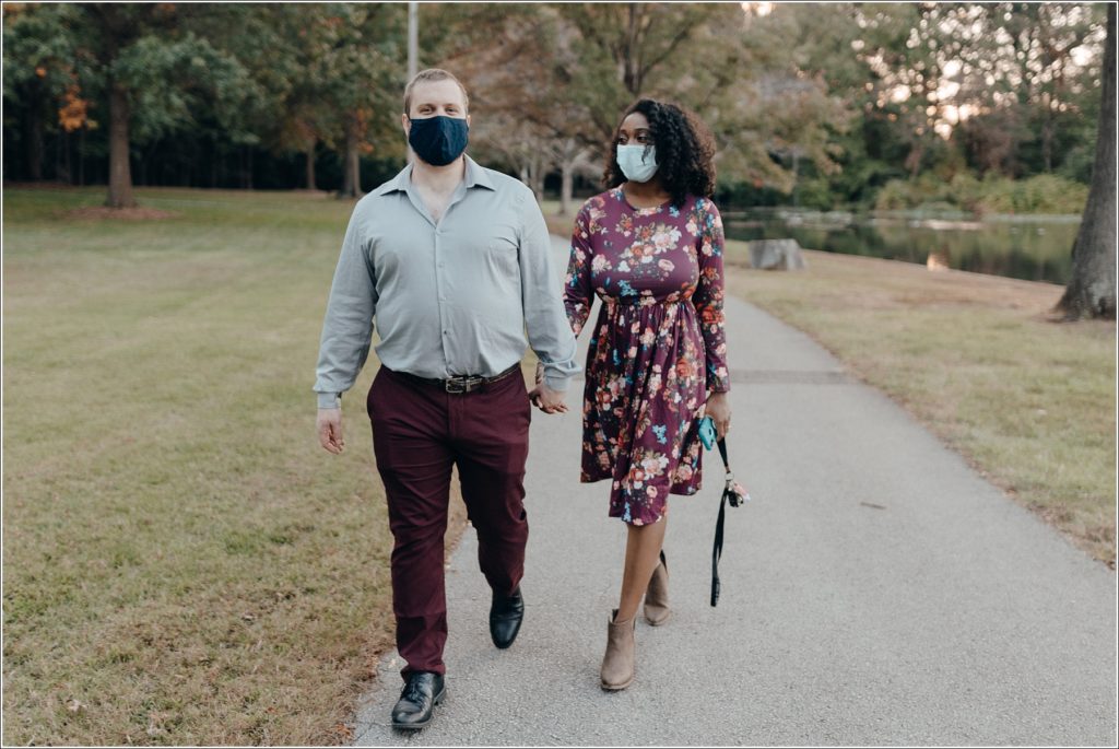 masked couple holds hands and walks with engagement photographers DC in Allen Pond Park