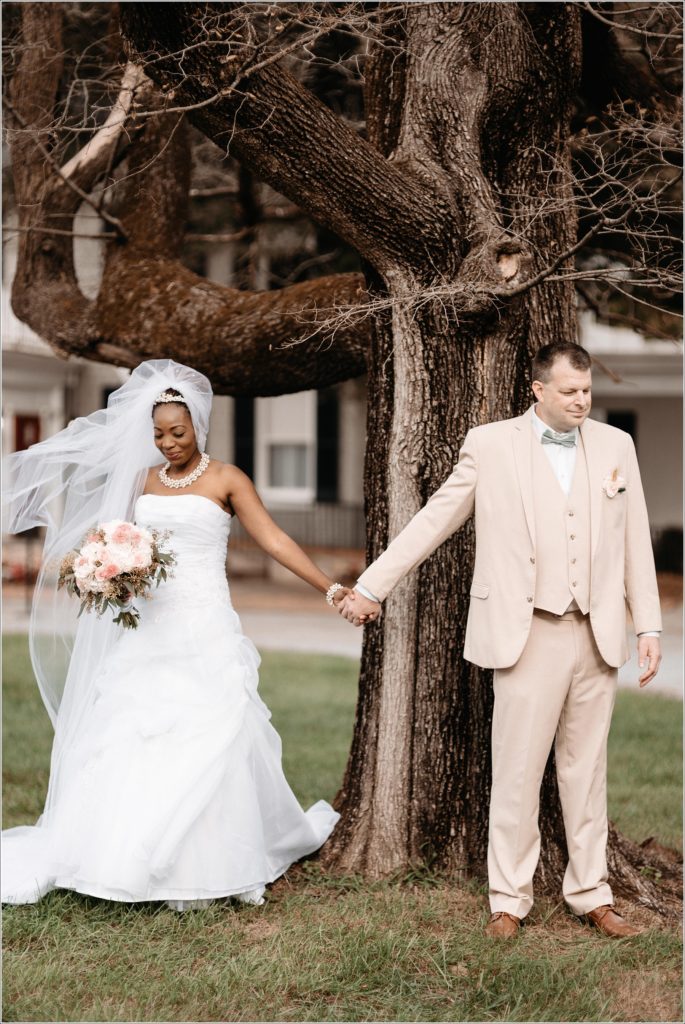 bride and groom hold hands at kings contrivance under tree for first look at wedding