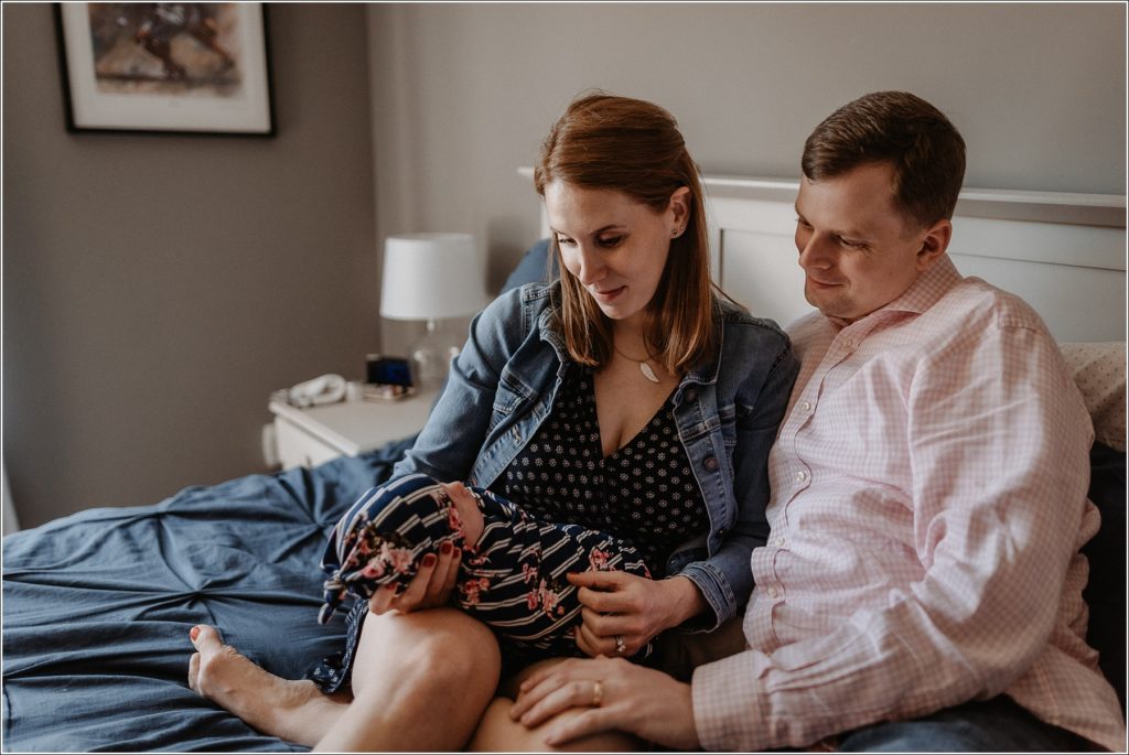 newborn and parents sit on bed captured by maryland newborn photographer