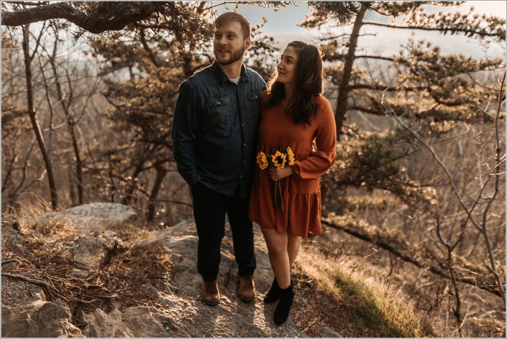 man and woman pose on rock at middletown overlook with sunflowers in burnt orange dress and blue jean button up at sunset