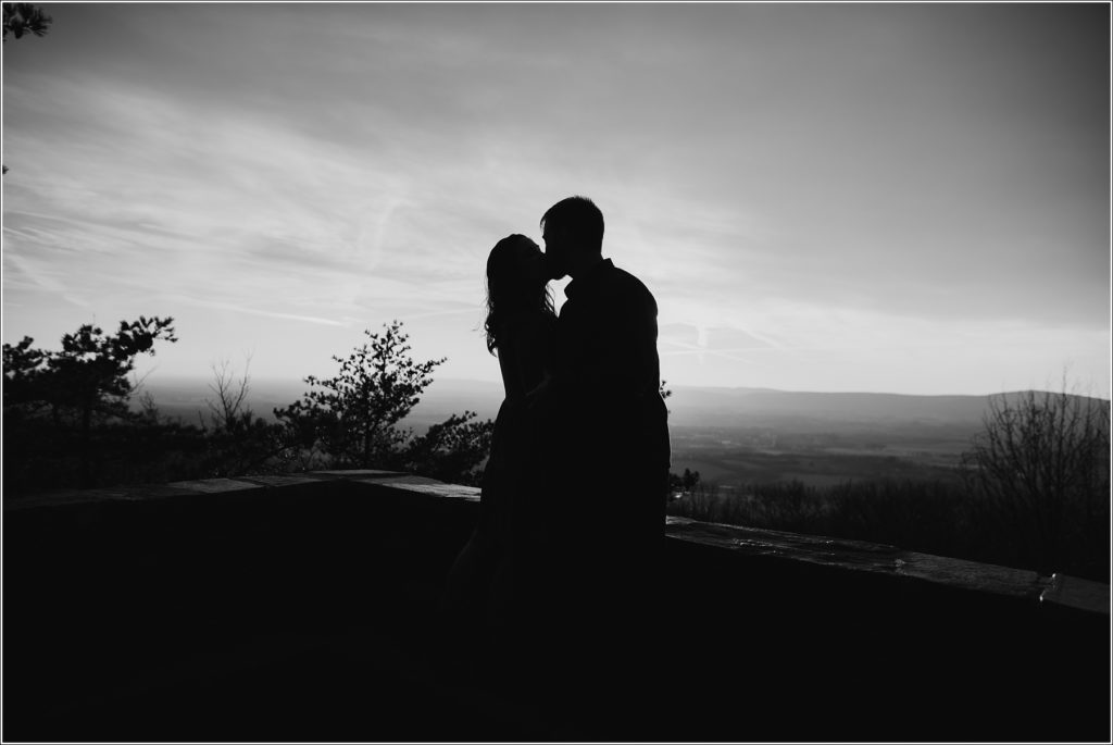 man and woman pose on rock at middletown overlook in burnt orange dress and blue jean button up at sunset black and white silhouette