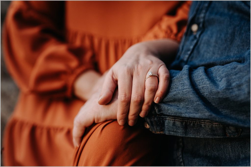 diamond engagement ring against burnt orange dress and blue jean shirt in golden light