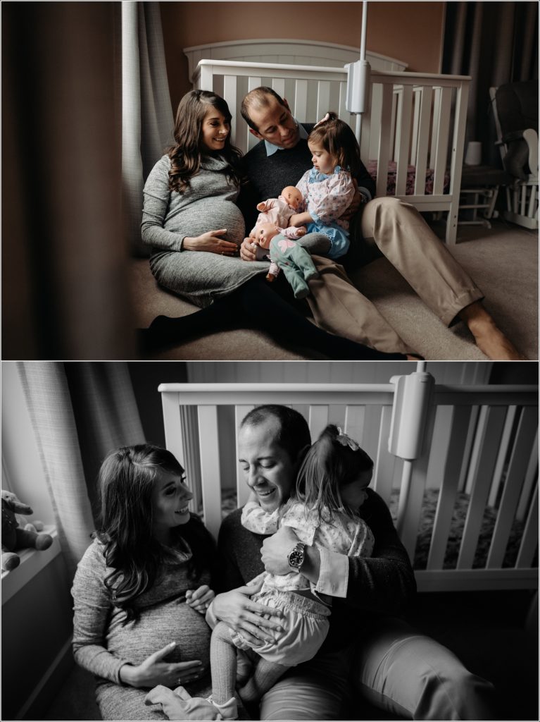 mom and dad and daughter sit near crib in window light for in home maternity photography