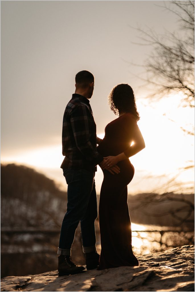 silhouette of couple posing with pregnant belly in red maternity dress and flannel shirt at sunset in Harper's Ferry with Maryland maternity photographer