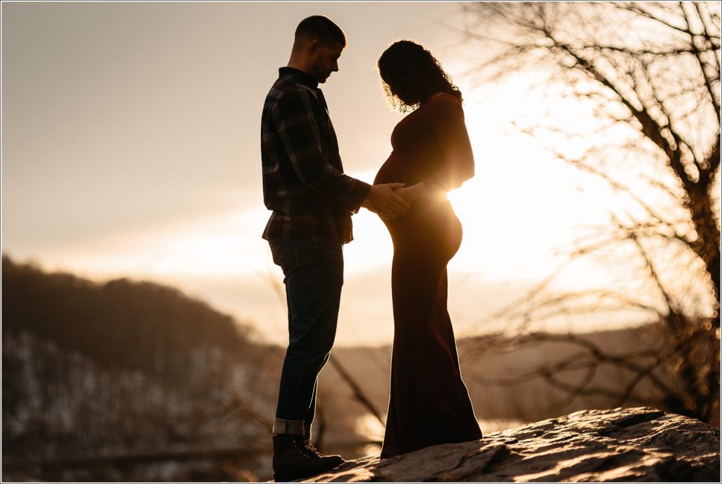 silhouette of couple posing with pregnant belly in red maternity dress and flannel shirt at sunset in Harper's Ferry with Maryland maternity photographer