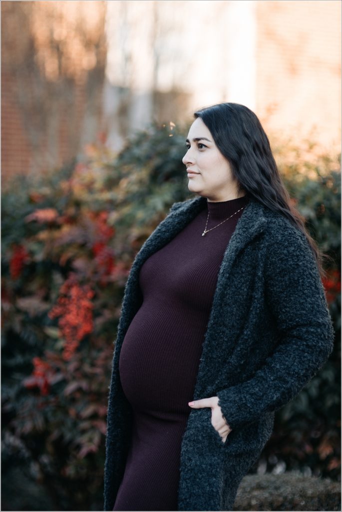 pregnant woman in purple maternity sweater dress and grey coat poses outside for Frederick winter maternity shoot