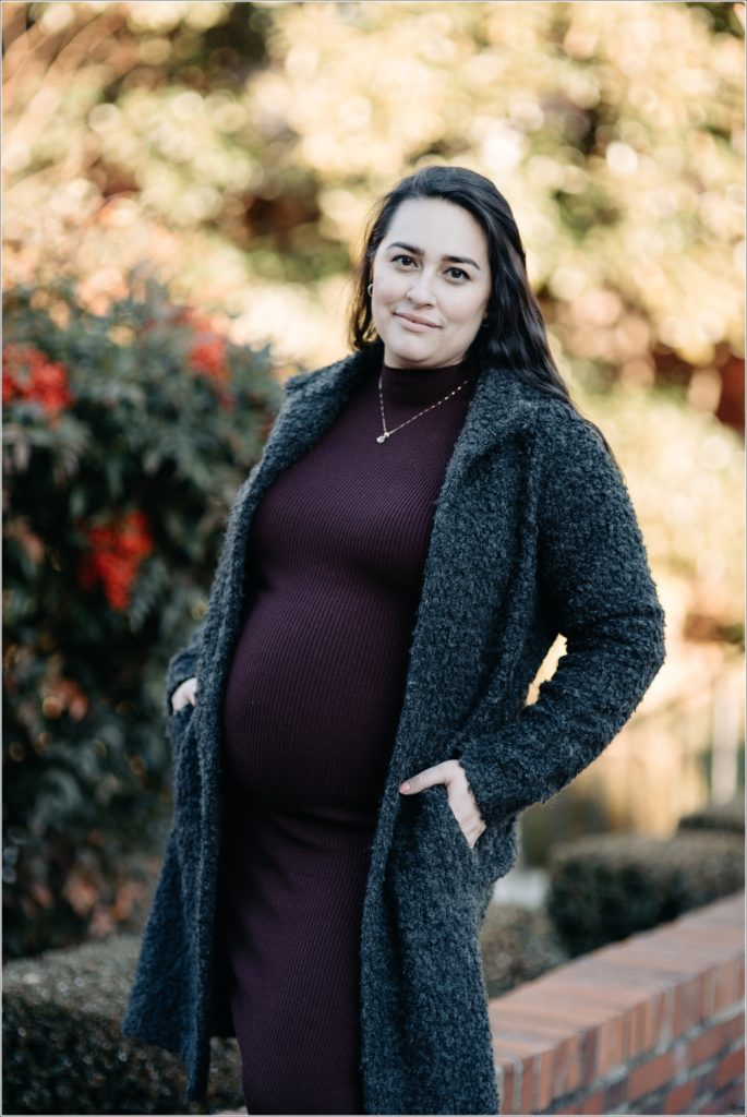 pregnant woman in purple maternity sweater dress and grey coat poses outside for Frederick winter maternity shoot