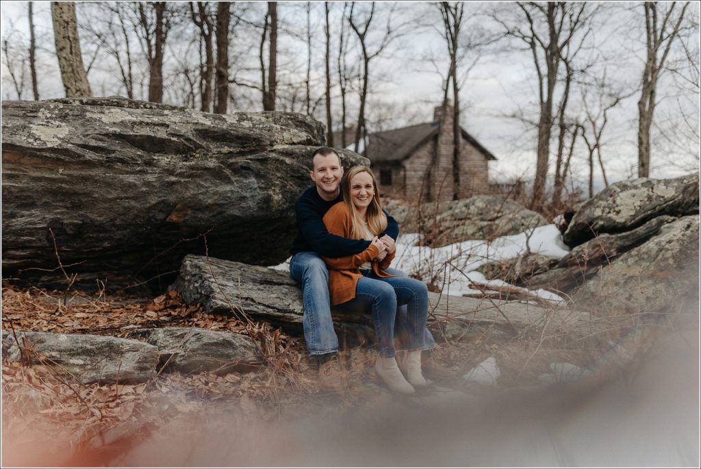 couple sits on a rock with snow on the ground at middletown overlook for firefighter engagement photos