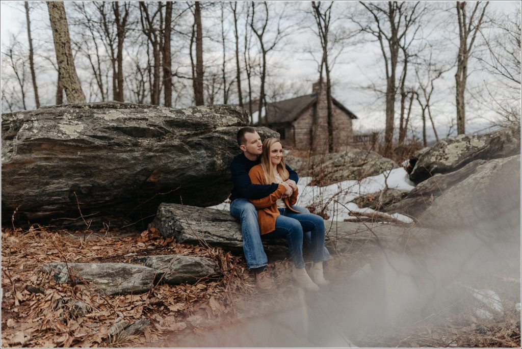 couple sits on a rock with snow on the ground at middletown overlook for firefighter engagement photos