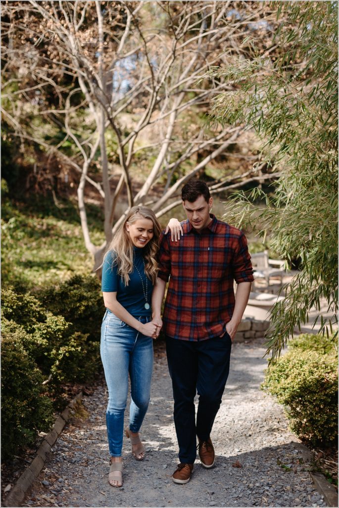 couple poses in asian garden for national arboretum engagement photos in red plaid and a teal turtleneck and jeans