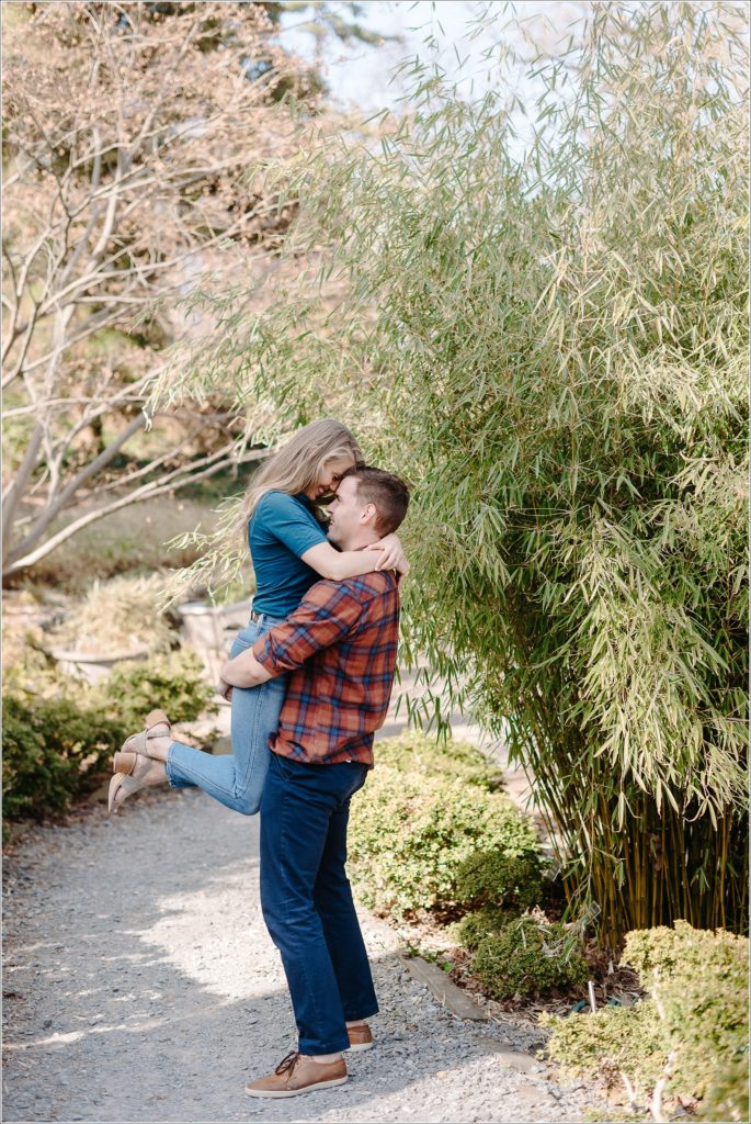 couple poses in asian garden for national arboretum engagement photos in red plaid and a teal turtleneck and jeans