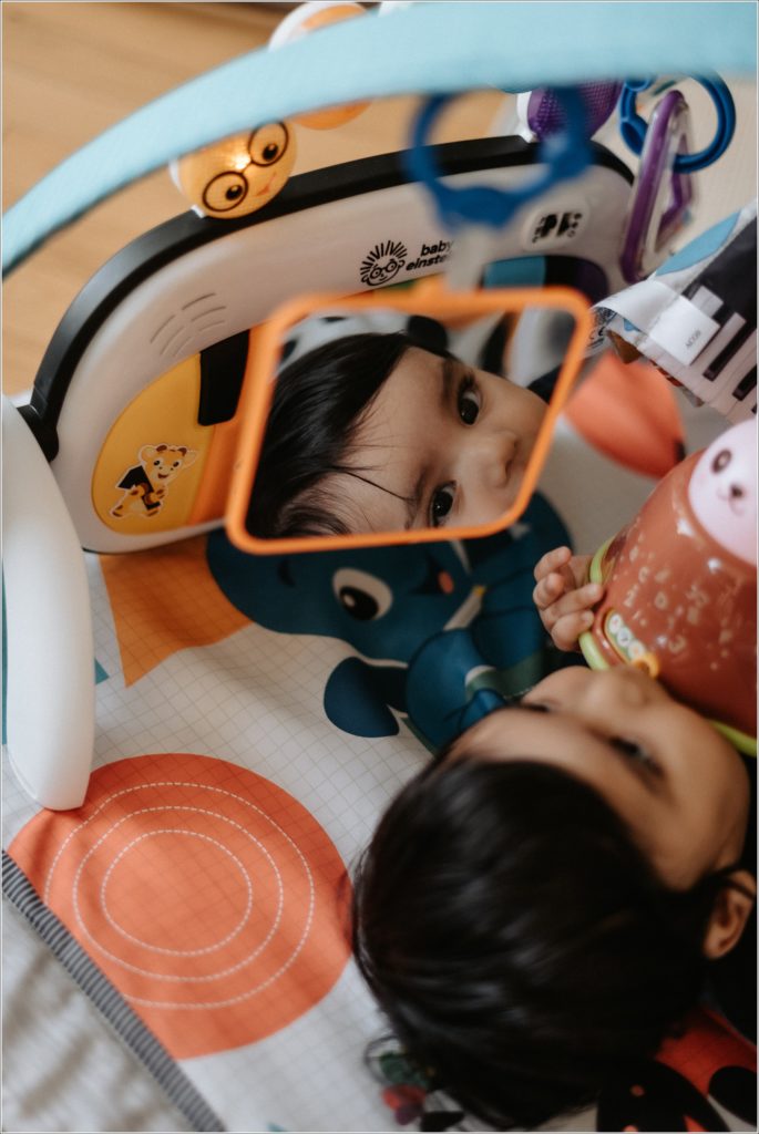 baby looks into mirror at camera laying on floor playmat