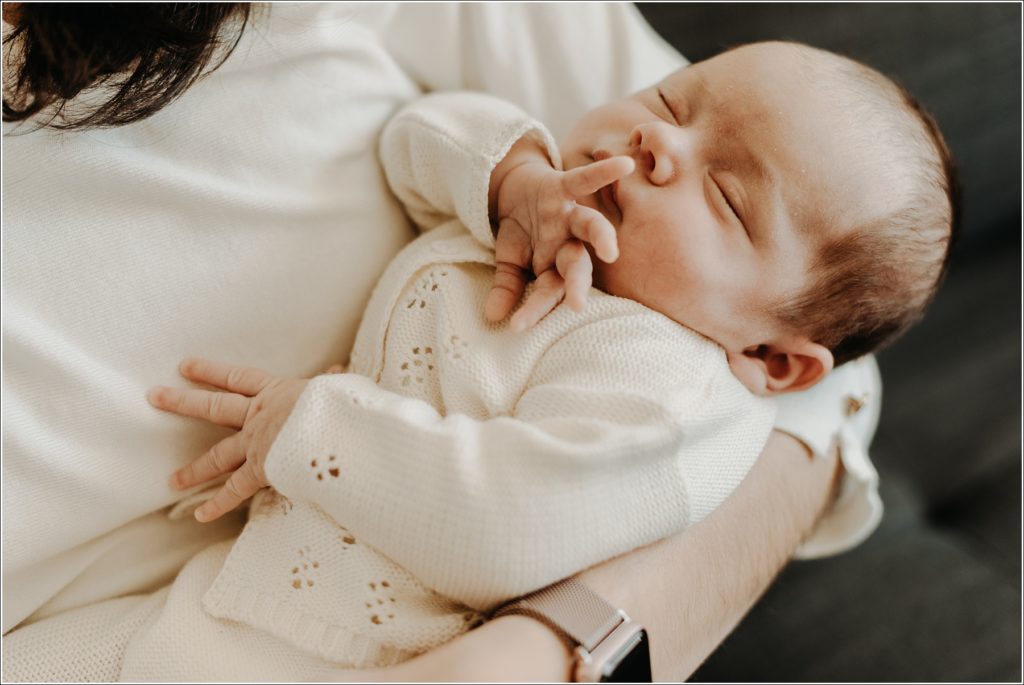 new mother holds newborn for in home newborn photography wearing cream sweater