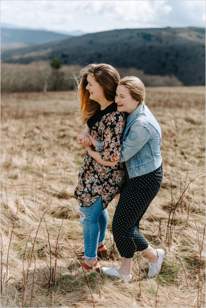two women embrace and laugh together on roan mountain in surprise proposal engagement photos