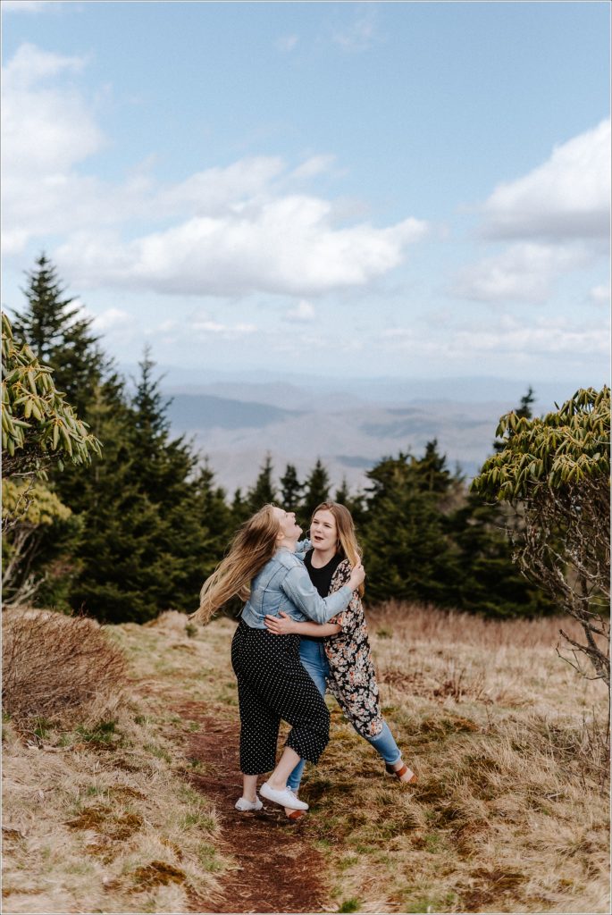 two women embrace and laugh with mountain backdrop on roan mountain carver's gap