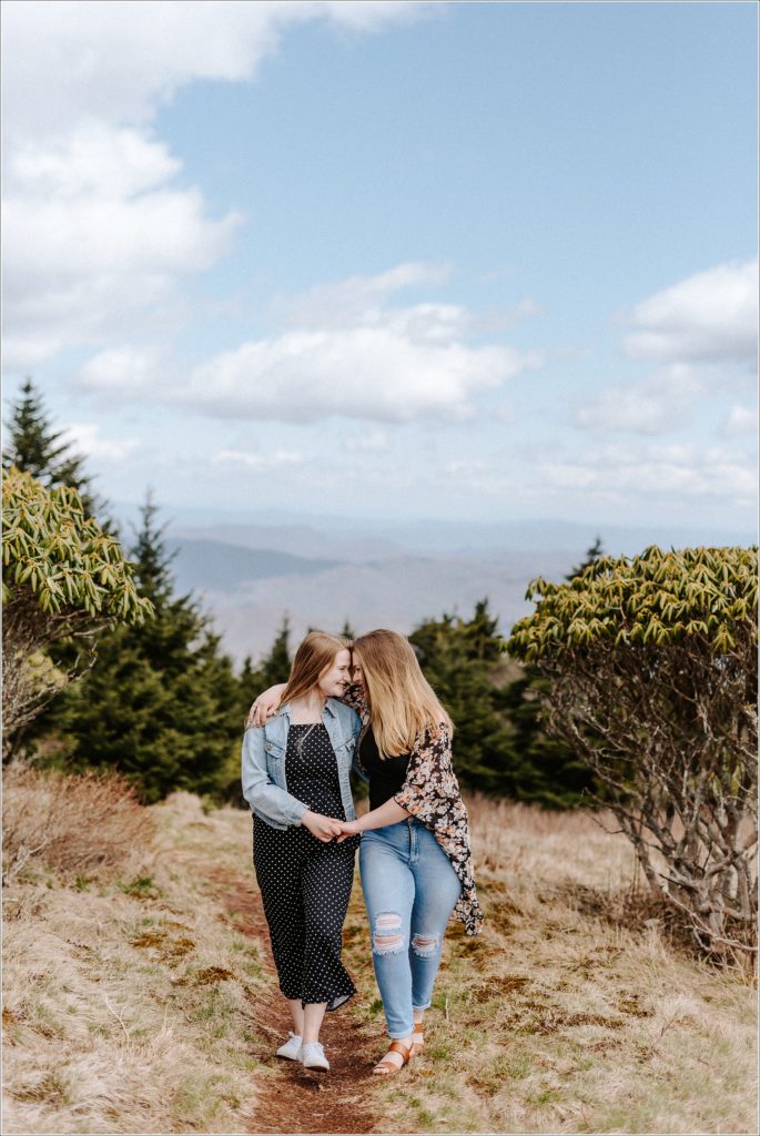 two women in jeans and floral and polka dots walk together on carver's gap roan mountain for surprise proposal
