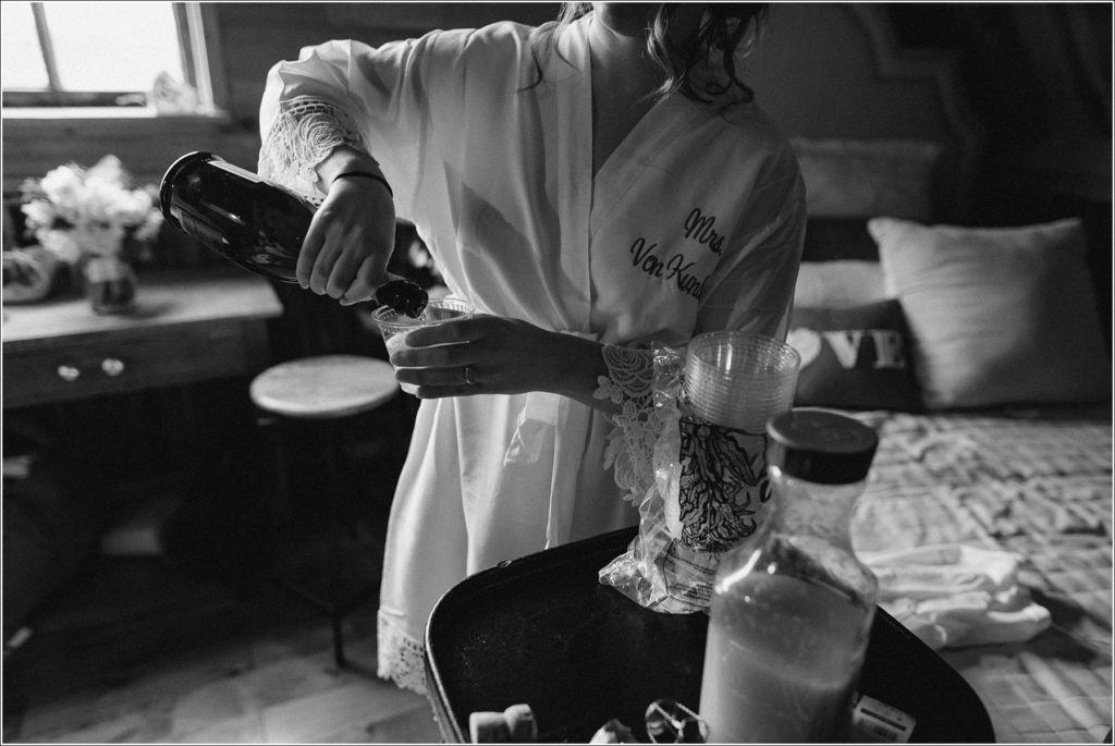 bride pours herself a mimosa in a silk robe in black and white