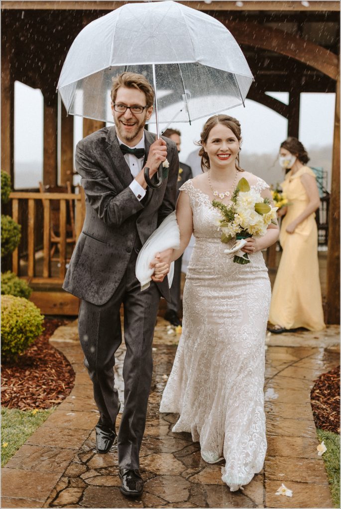 bride and groom walk down the aisle with an umbrella at the barns at chip ridge