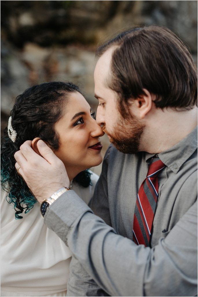couple snuggles up at great falls virginia for photoshoot in white dress and grey button up shirt
