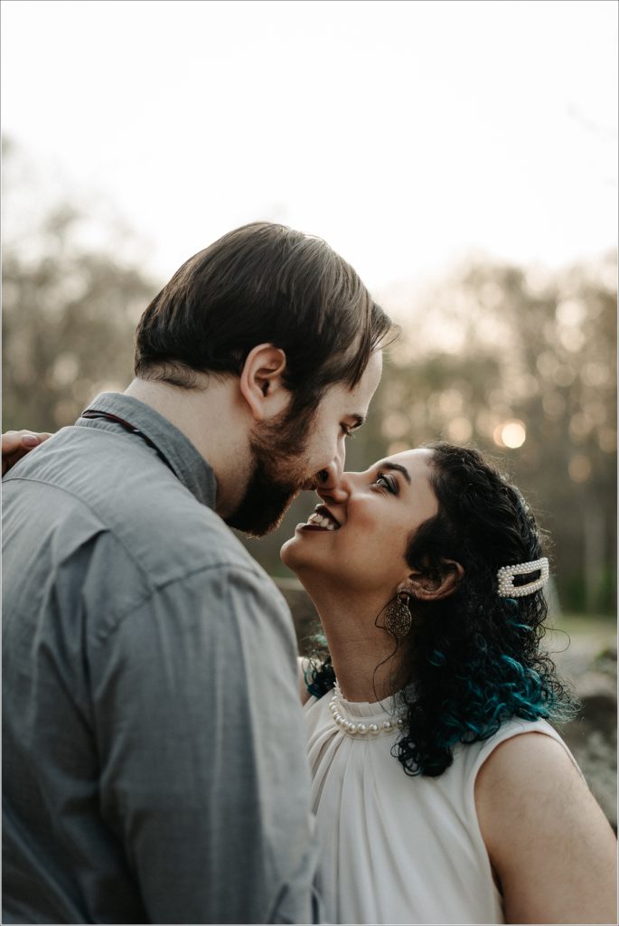 couple snuggles up in white dress and pearls and grey shirt at sunset for dc photoshoot