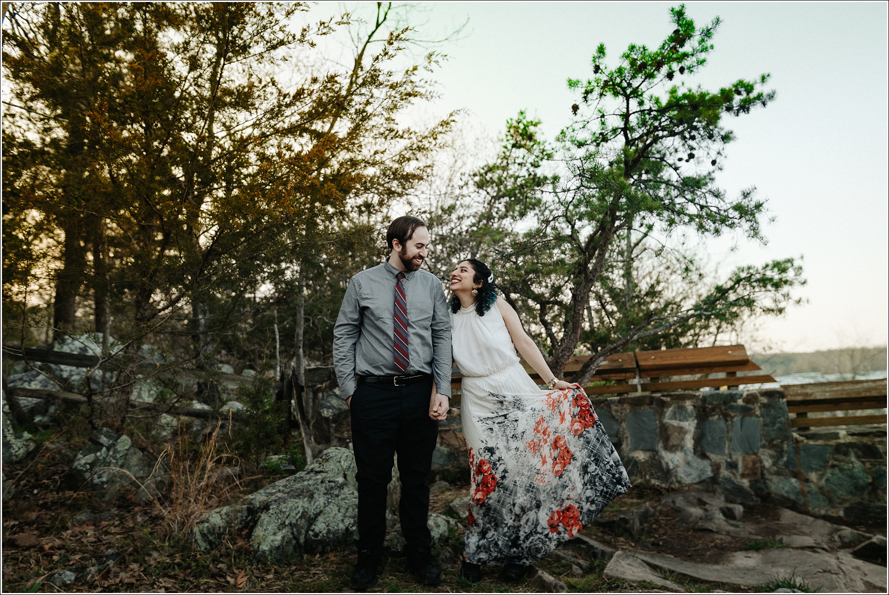 couple snuggles up at sunset with grey button and red tie and white dress with pearls at great falls state park for photoshoot
