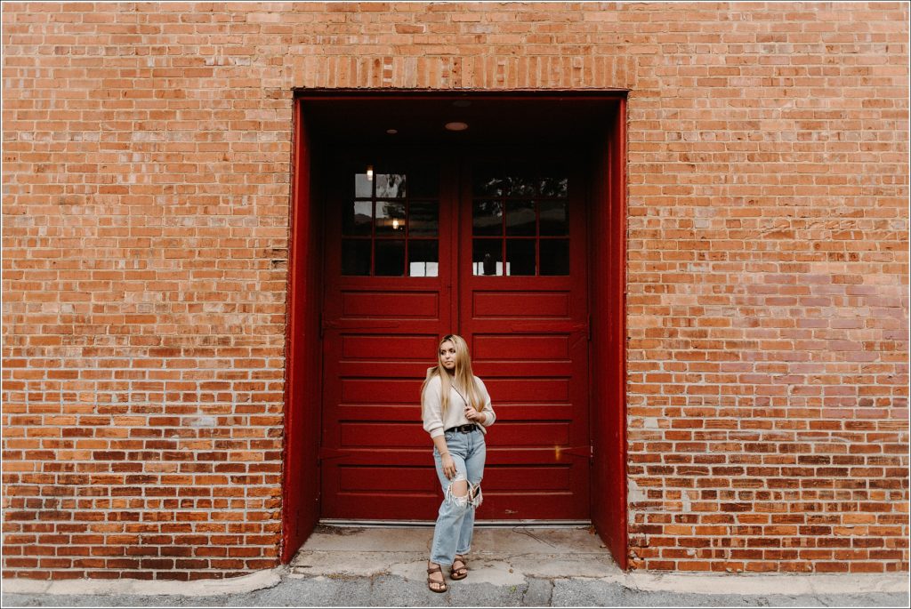 girl stands framed by big red double doors in downtown Frederick alleyway for senior pics ideas