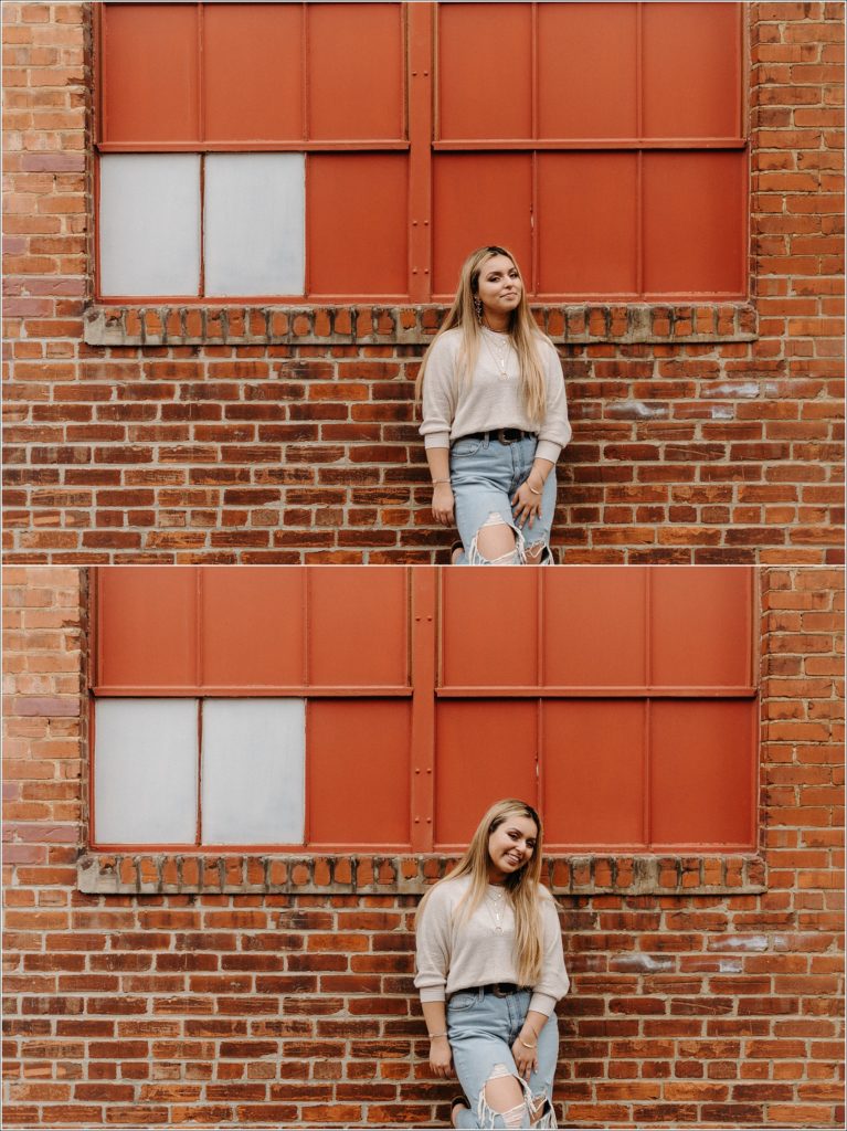 girl stands in front of red windows in sweater and jeans in downtown Frederick alleyway