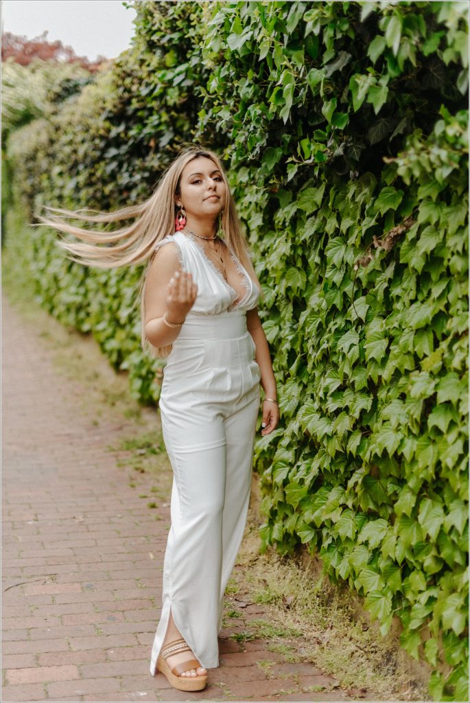 teenager poses in white jumpsuit near wall of vines in Downtown Frederick