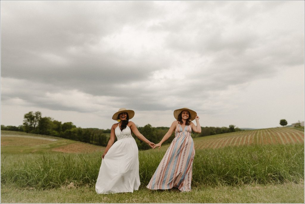 best friends photoshoot holding hands in sundresses in field at linganore winery with stormy sky