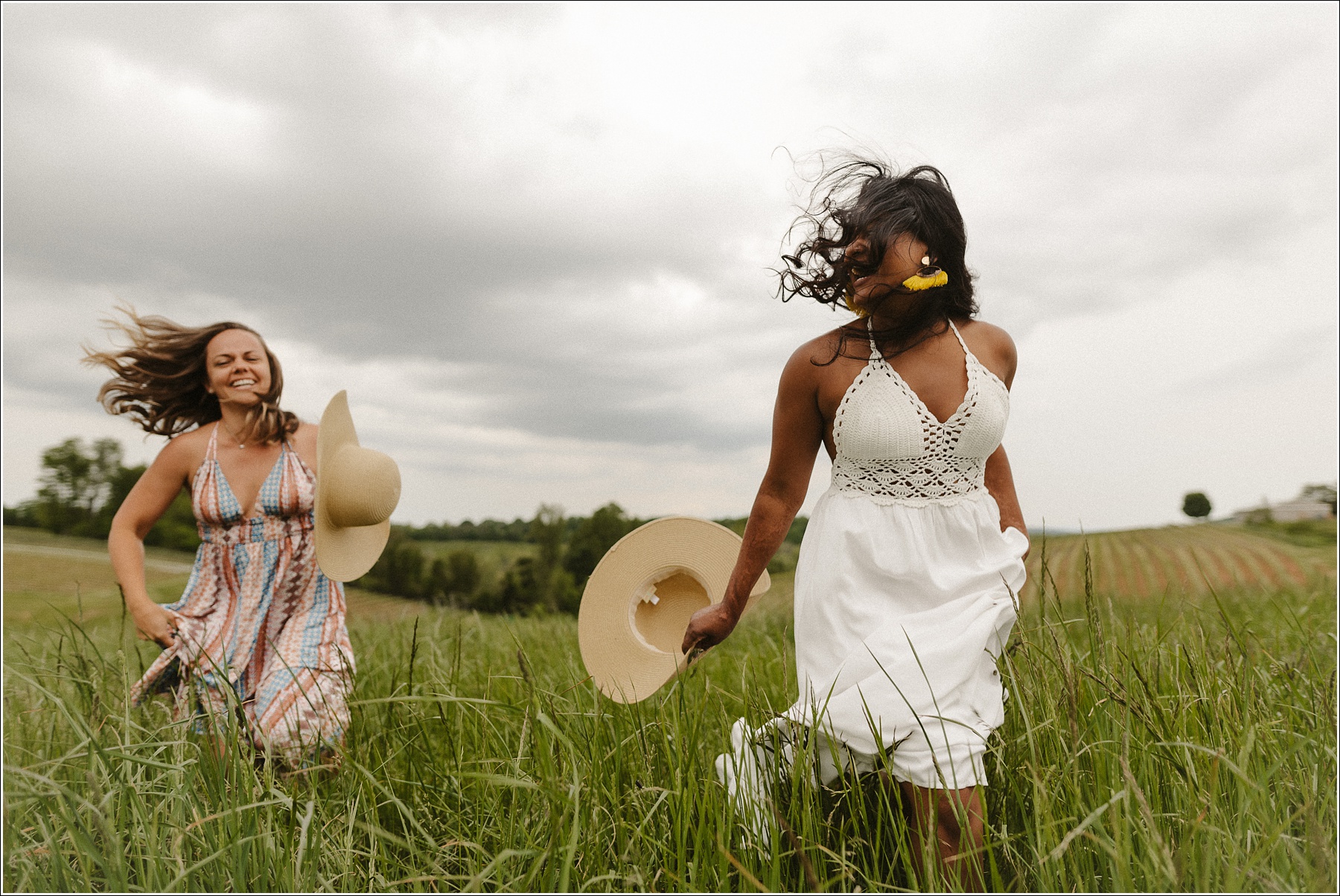 best friends run in sundresses in field at linganore winery with stormy sky