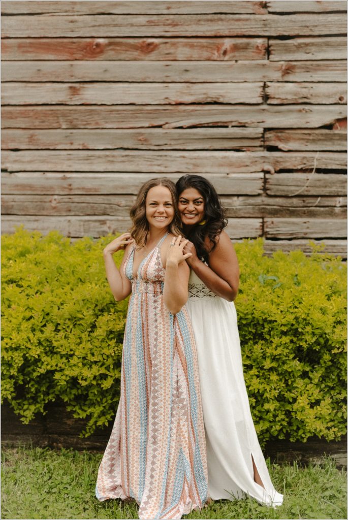 women in sundresses pose in front of red barn and green bushes in best friends photoshoot at linganore winery