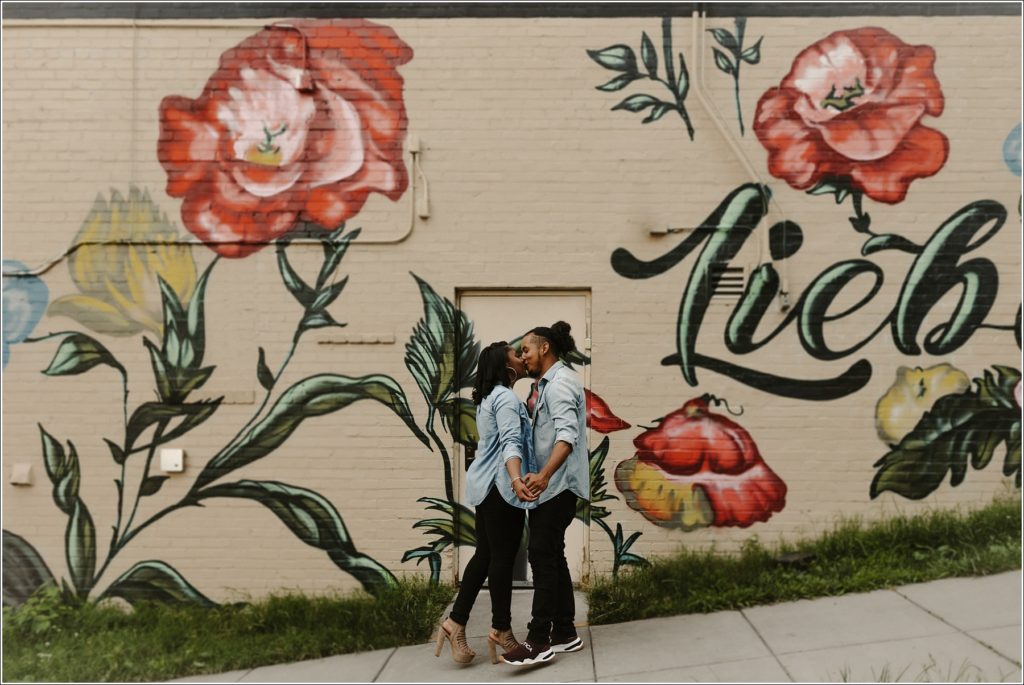 couple poses for dc engagement photographer in georgetown in floral dress and striped shirt against mural wall at berliner