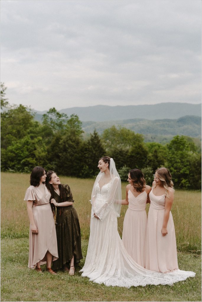 bride and bridesmaids laugh together in field in front of northeast tennessee mountains